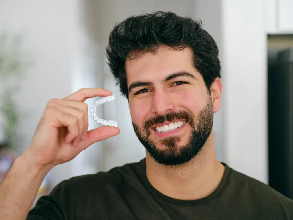Smiling person holding an Invisalign used for orthodontic teeth straightening in Monett, MO
