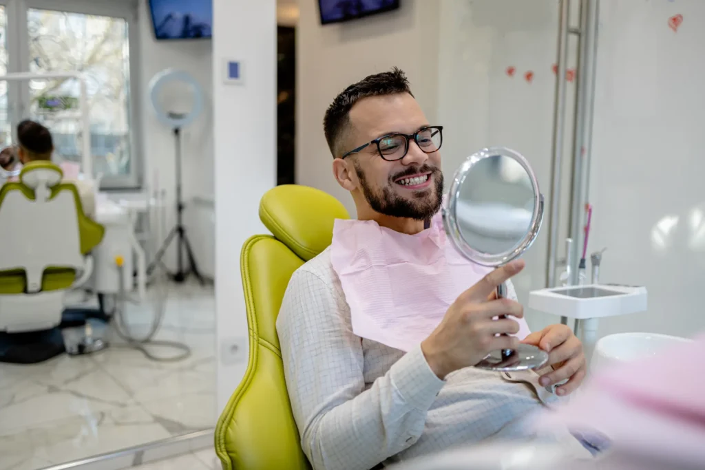 Smiling patient holding a mirror in a dental chair after cosmetic treatment in Monett, MO