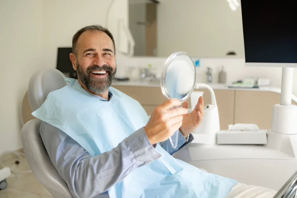 Patient seated in a dental chair holding a mirror after teeth whitening treatment in Monett, MO
