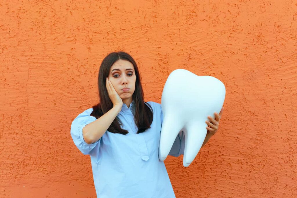 Person holding large tooth model and touching cheek to illustrate tooth pain and dental issues in Monett, MO