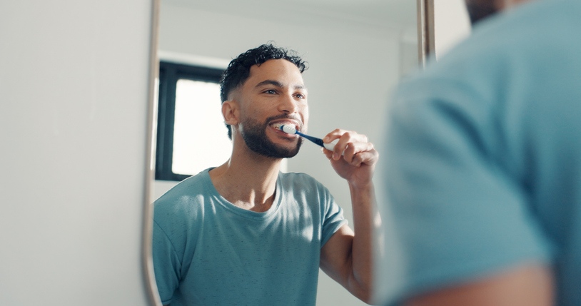 Brushing teeth in a mirror for a daily oral care routine in Monett, MO